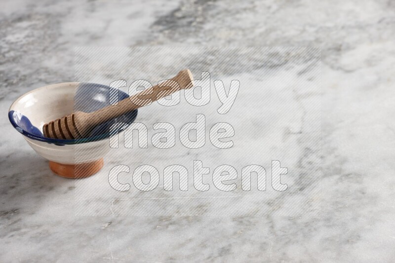 وعاء فخاري متعدد الألوان مع ملعقة عسل خشبية بداخله على خلفية من الرخام الرمادي