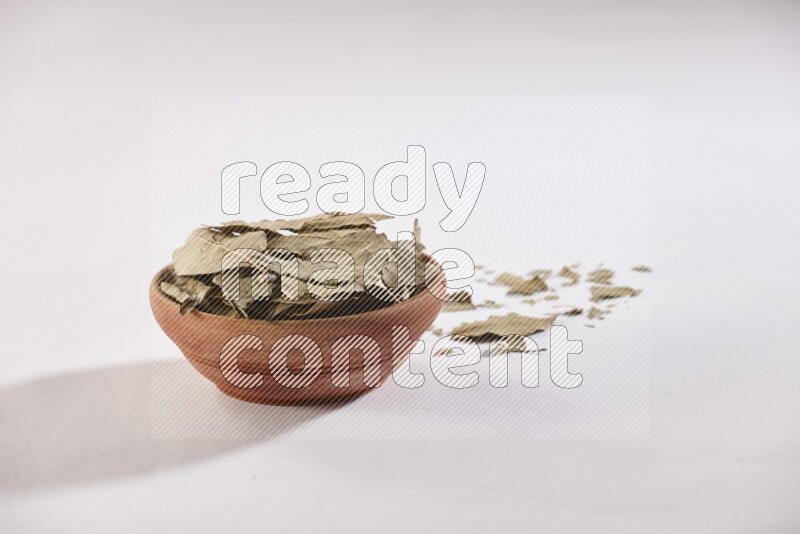 A wooden bowl filled with dried bay leaves on white flooring in different angles
