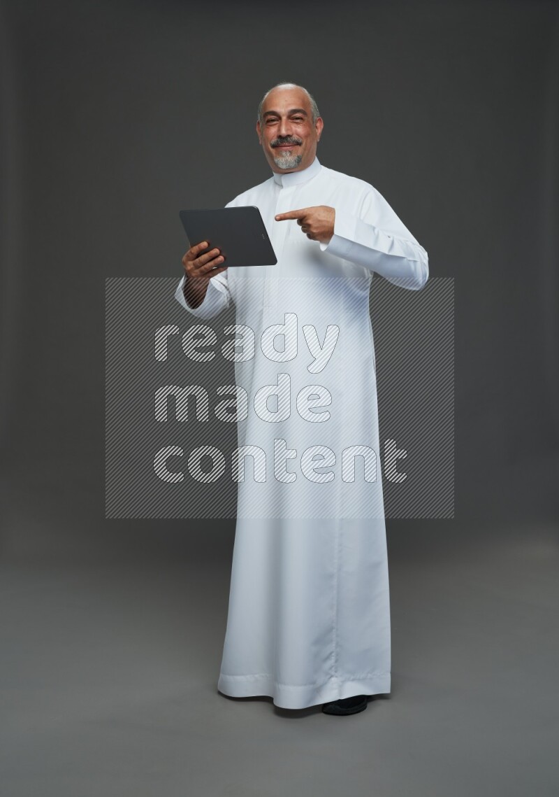 Saudi man without shomag Standing working on tablet on gray background