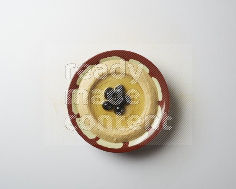 Hummus in a traditional plate garnished with black olives on a white background