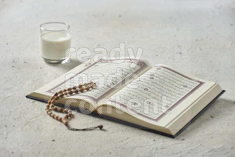 Quran with dates, prayer beads and different drinks all placed on textured white background