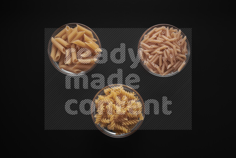Different pasta types in glass bowls on black background