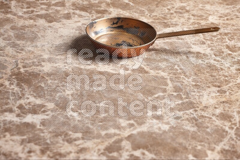 A small copper pan on beige marble background