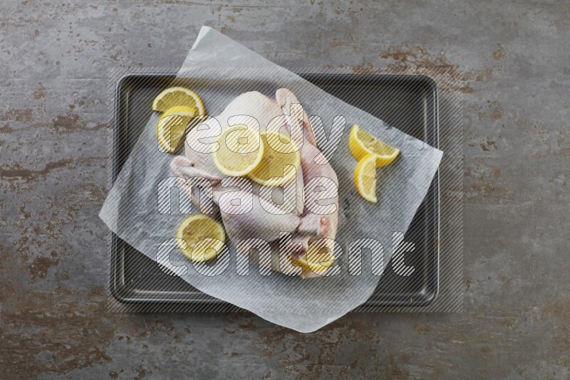 whole raw chicken on an oven trey direct on a rustic grey background