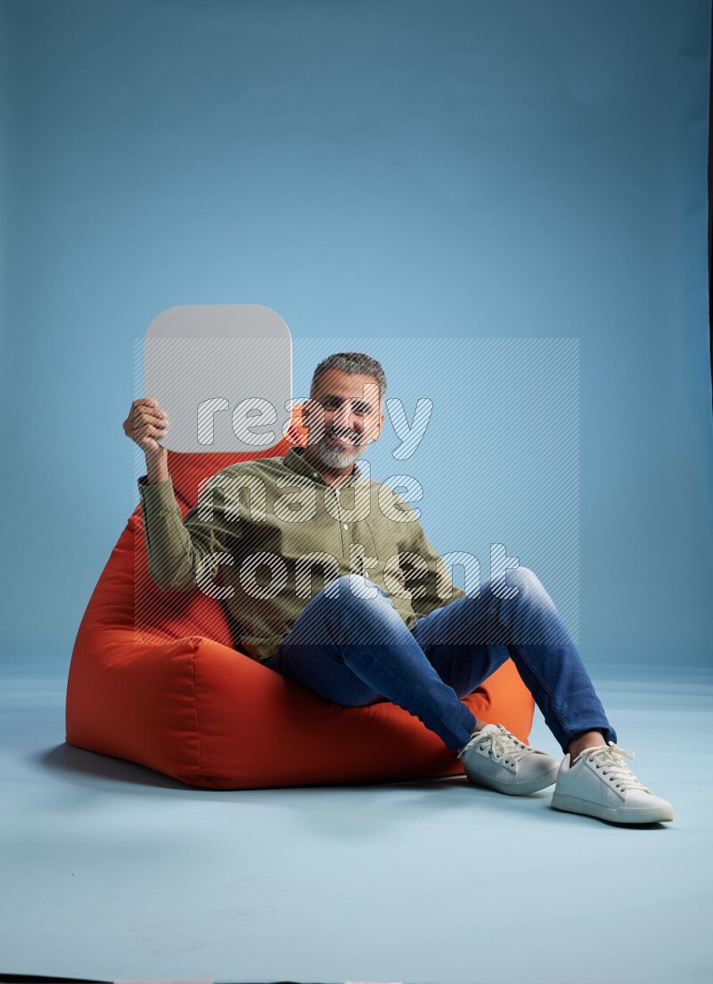 A man sitting on a orange beanbag and holding social media sign