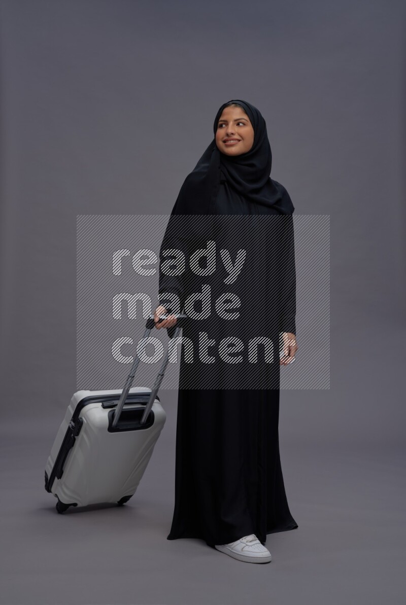 Saudi woman wearing Abaya standing holding bag on gray background