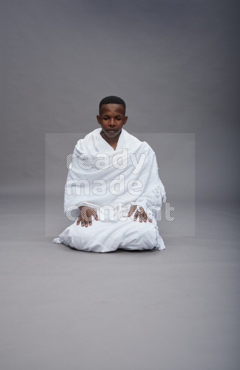 A man wearing Ehram sitting on floor praying on gray background