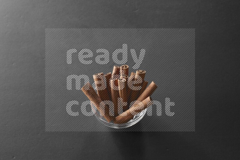 A glass bowl full of cinnamon sticks on black flooring