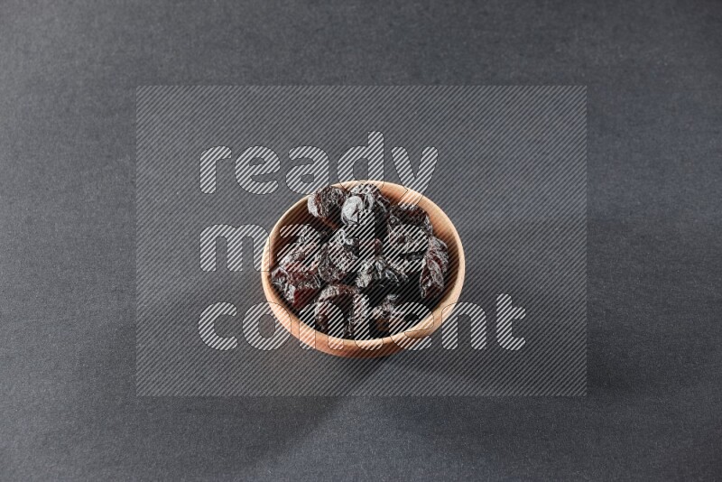 A wooden bowl full of dried plums on a black background in different angles