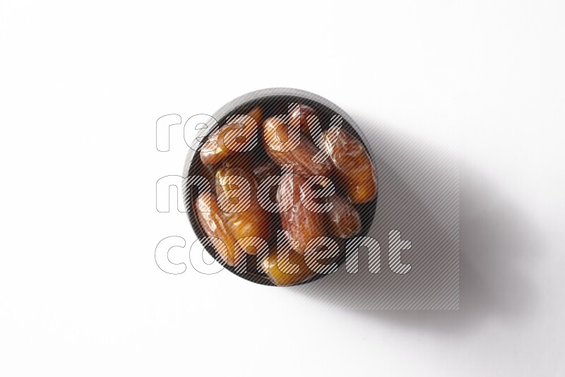 Dates in a black pottery bowl on white background
