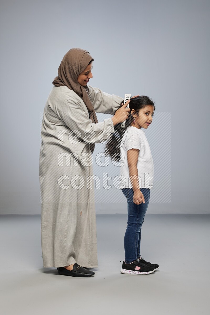 Mom standing styling hair for her daughter on gray background
