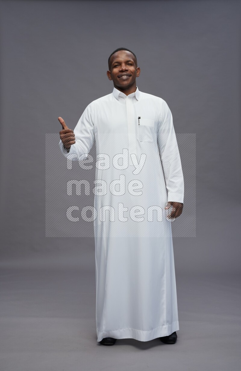 Saudi man wearing thob standing interacting with the camera on gray background