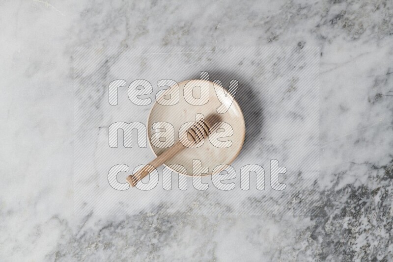 Beige pottery plate with wooden honey dipper in it on grey marble background