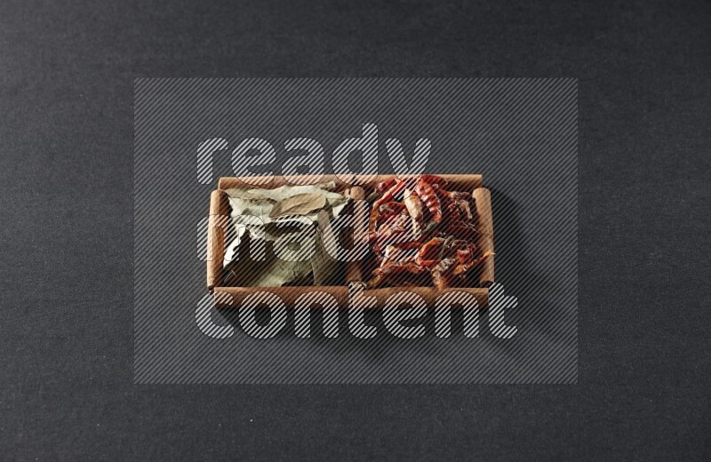 مربعان من أعواد القرفة ممتلئان بالفلفل الحار المجفف وأوراق الغار علي خلفية سوداء