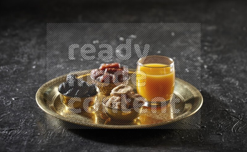 Dried fruits in metal bowls with qamar eldin on a tray in dark setup