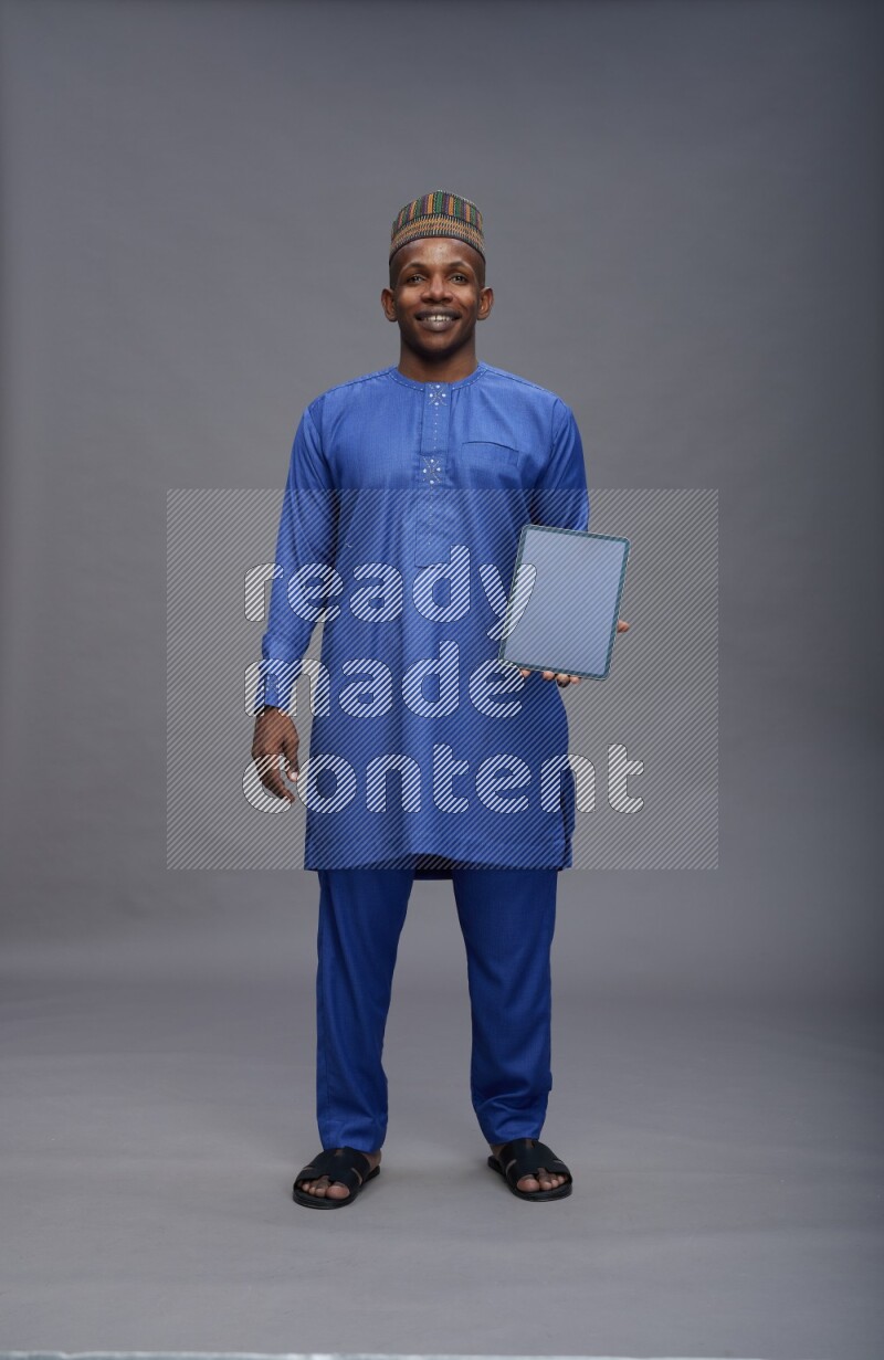Man wearing Nigerian outfit standing showing tablet to camera on gray background
