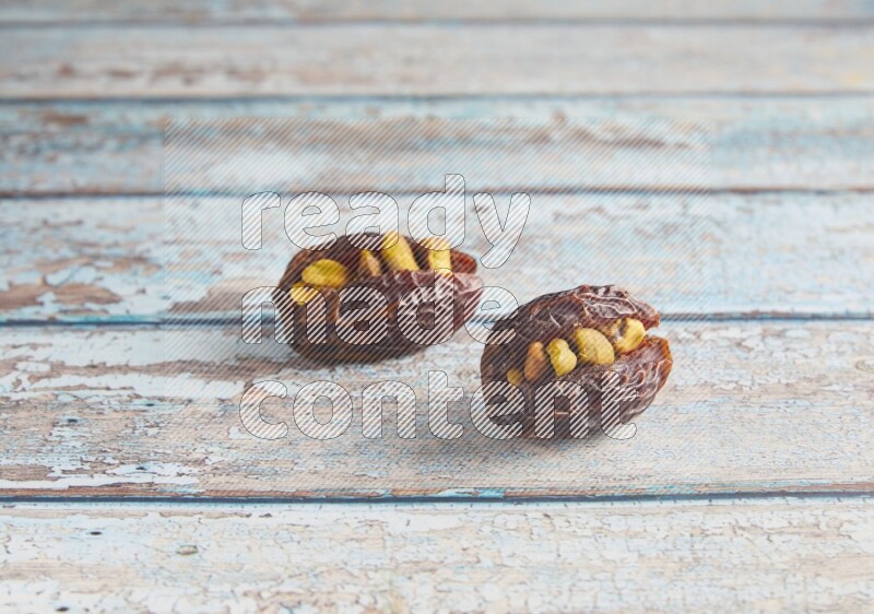 two pistachio stuffed madjoul dates on a light blue wooden background