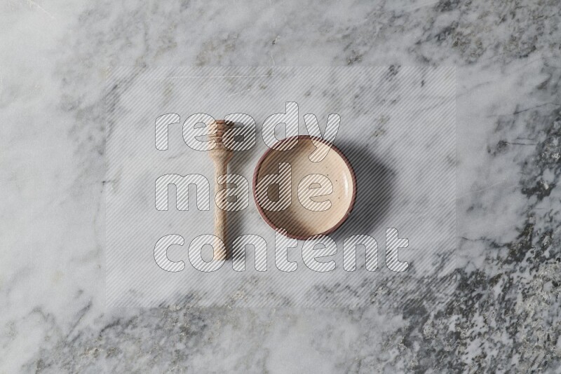 Beige pottery oven bowl with wooden honey dipper on the side on grey marble background