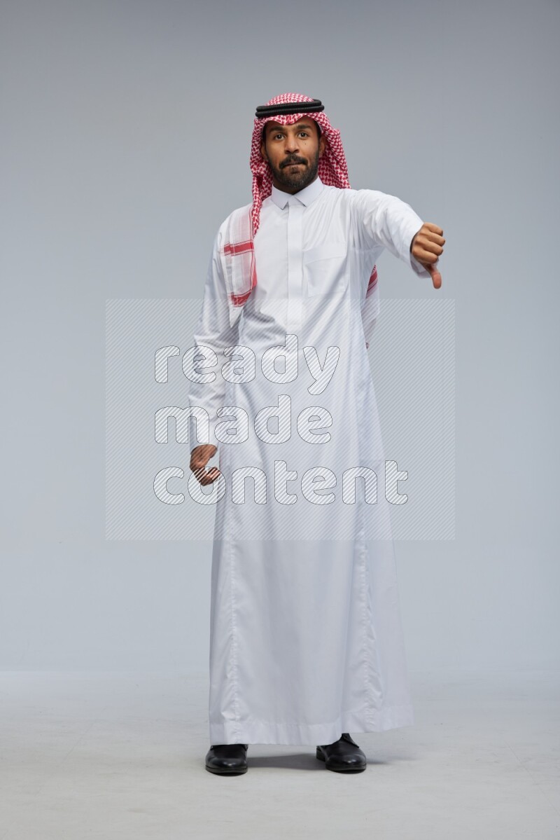 Saudi man Wearing Thob and shomag standing interacting with the camera on Gray background