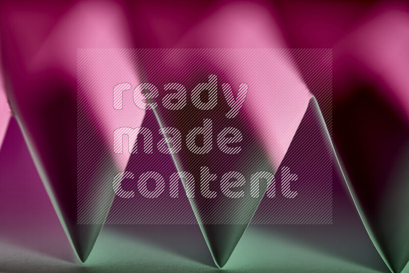 A close-up abstract image showing sharp geometric paper folds in green and purple gradients