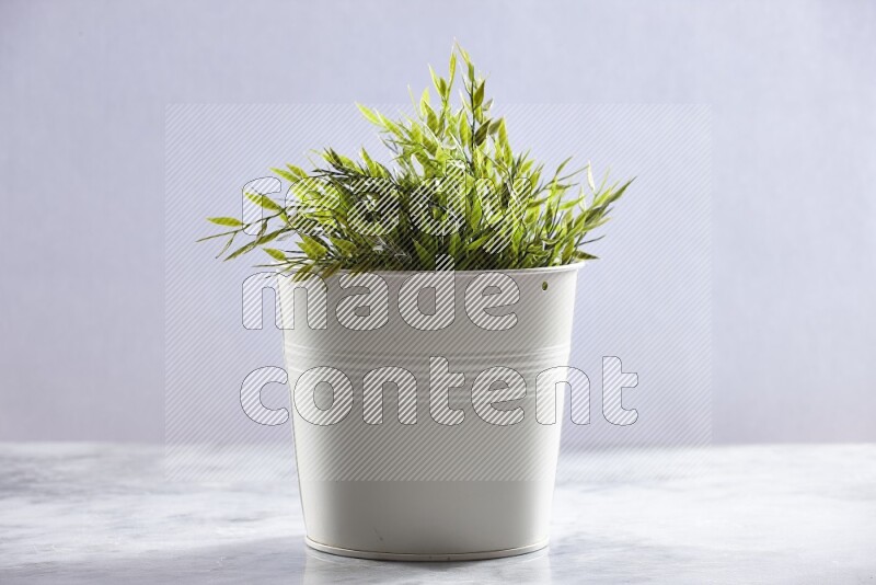 Green artificial plant in white pot on grey marble background