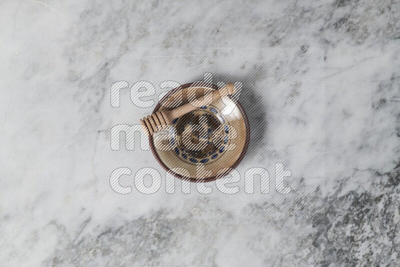 Decorative pottery plate with wooden honey dipper in it on grey marble background