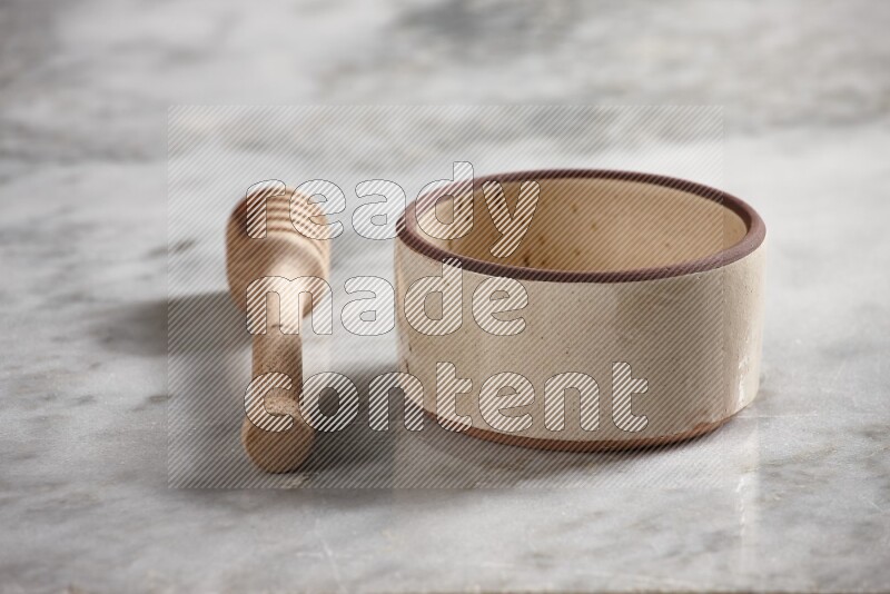 Beige pottery oven bowl with wooden honey dipper on the side on grey marble background