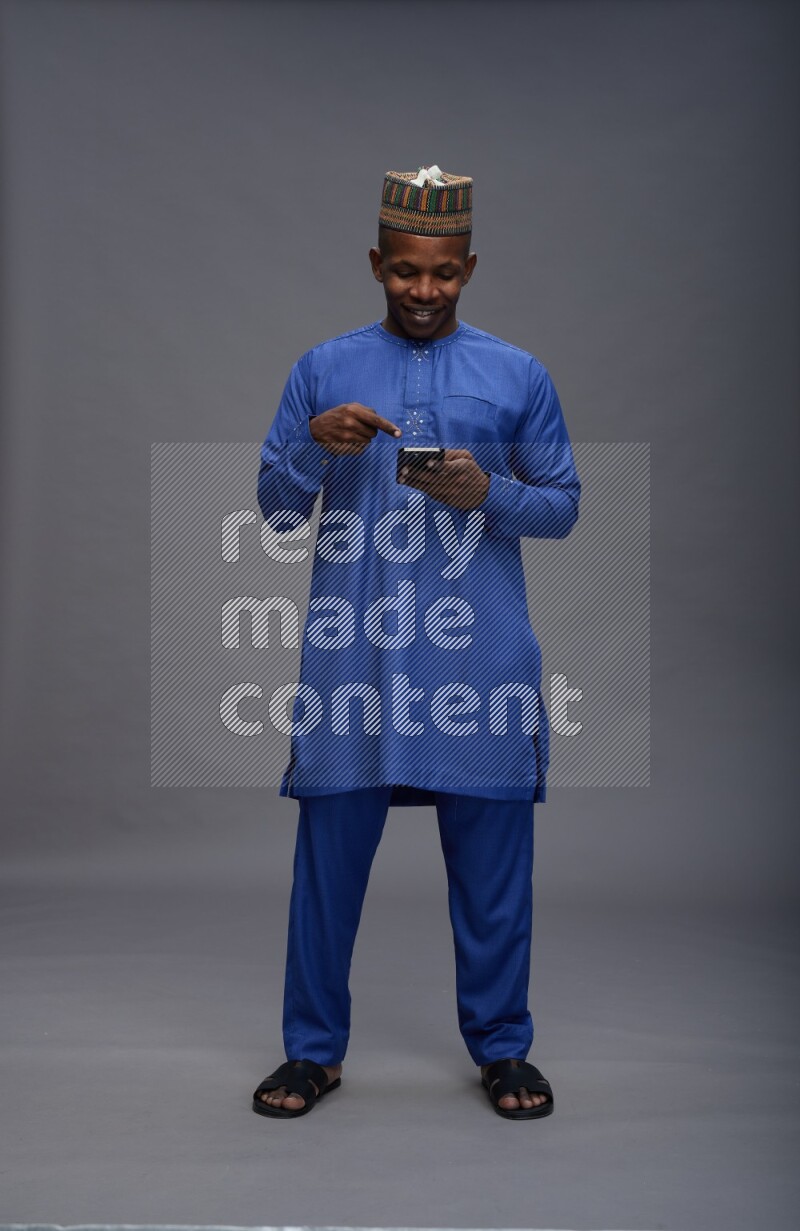 Man wearing Nigerian outfit standing texting on phone on gray background
