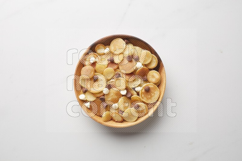 Top-view shot of mixed chocolate chips cereal pancakes in a round bowl on white background
