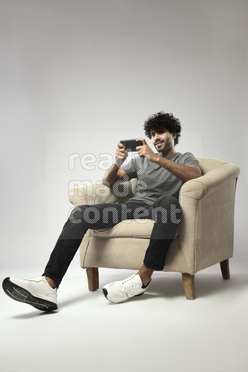 A man wearing casual sitting on a chair gaming on the phone on white background