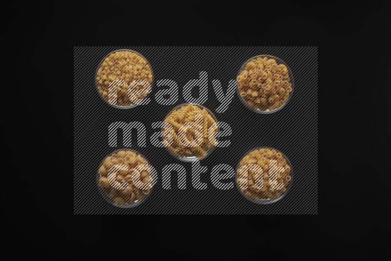 Different pasta types in 5 glass bowls on black background