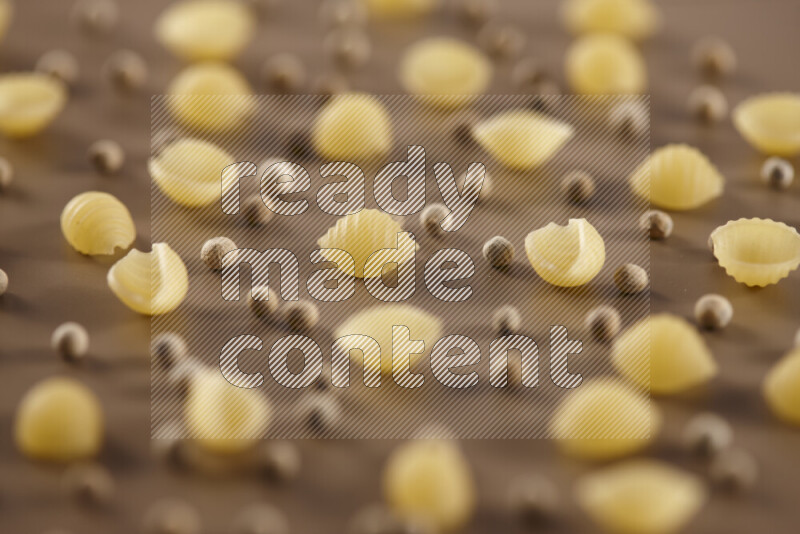 Raw pasta with different ingredients such as cherry tomatoes, garlic, onions, red chilis, black pepper, white pepper, bay laurel leaves, rosemary and cardamom on beige background