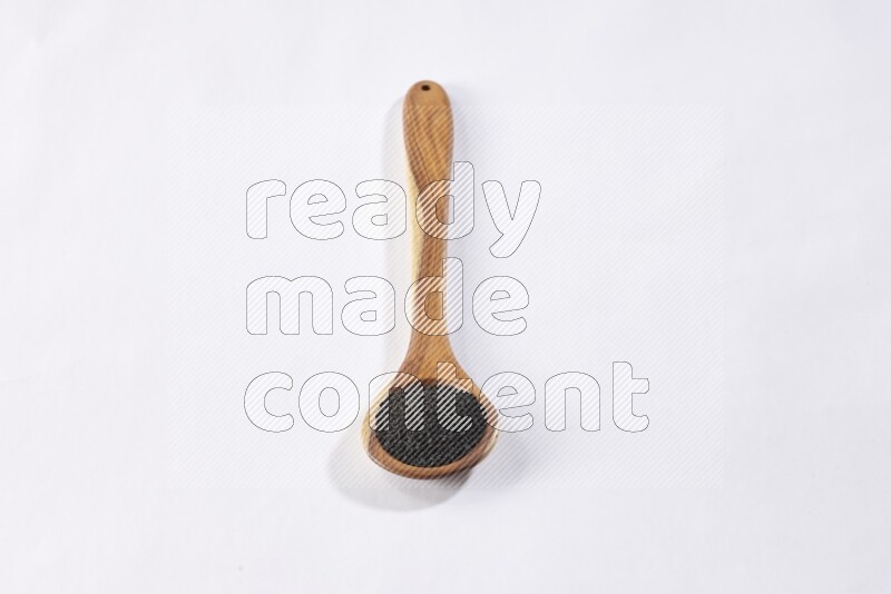 A wooden ladle full of black seeds on a white flooring