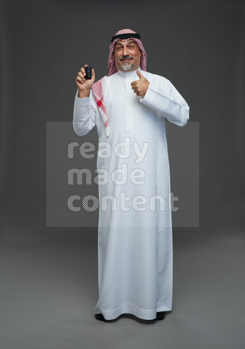 Saudi man with shomag Standing holding car key on gray background