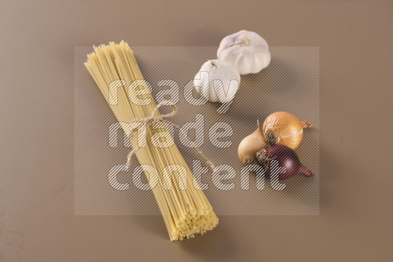 Raw pasta with different ingredients such as cherry tomatoes, garlic, onions, red chilis, black pepper, white pepper, bay laurel leaves, rosemary and cardamom on beige background