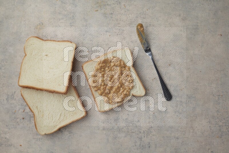 crunchy peanut butter on white toast and white toast slices on a light blue textured background