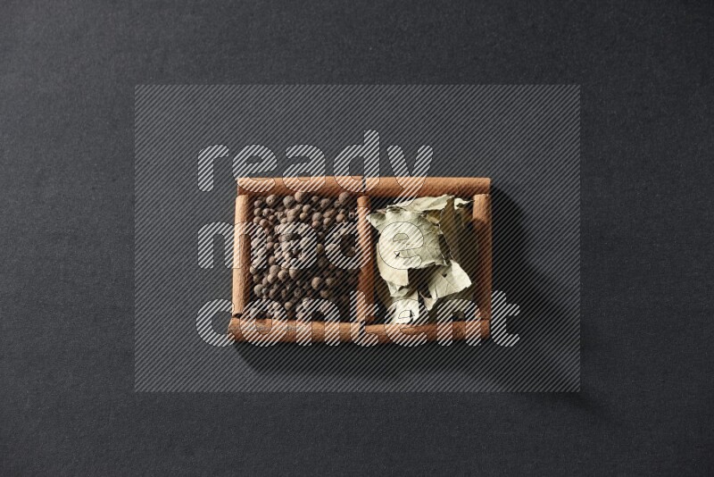 مربعان من أعواد القرفة ممتلئان ببهار الفلفل الحلو وأوراق الغار علي خلفية سوداء