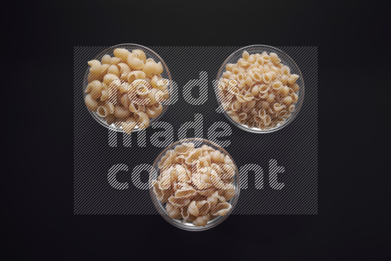 Different pasta types in glass bowls on black background