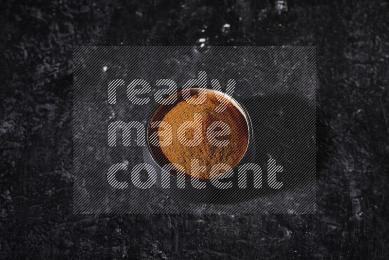 A black pottery bowl full of ground paprika powder on black background