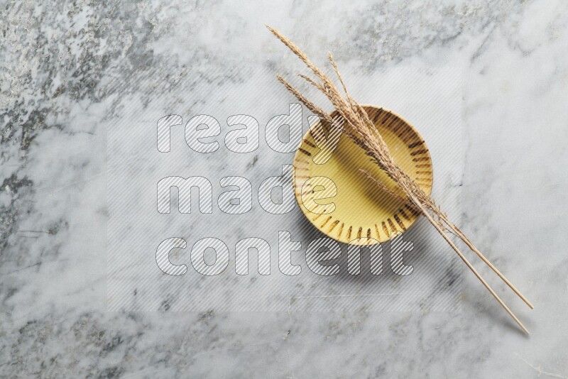 Wheat stalks on multicolored pottery plate on grey marble background
