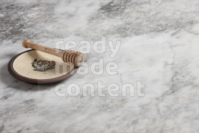 Decorative pottery plate with wooden honey dipper in it on grey marble background