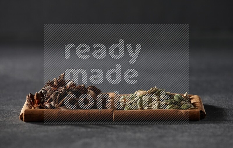 مربعان من أعواد القرفة ممتلئان بحبوب الهيل واليانسون النجمي علي خلفية سوداء