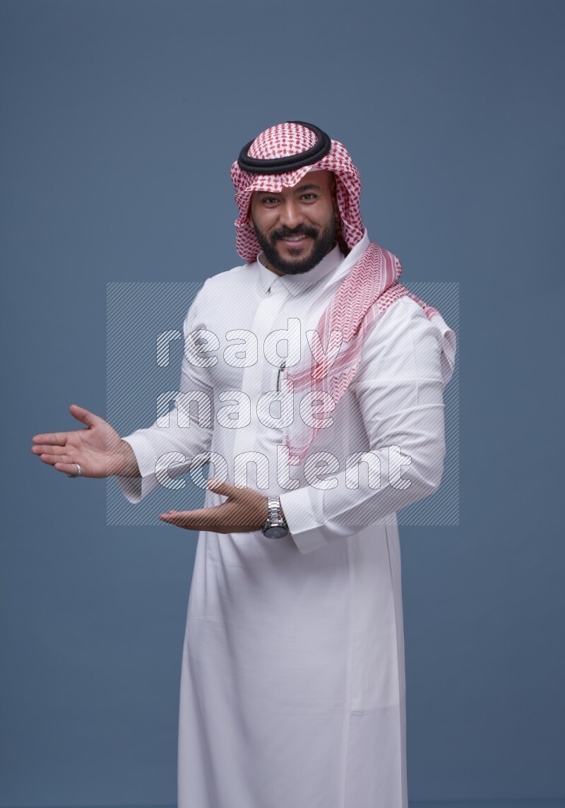 A man pointing on blue background wearing Saudi Thob with Shomag
