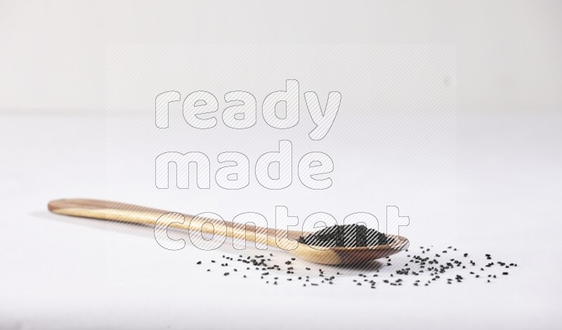 A wooden ladle full of black seeds on a white flooring