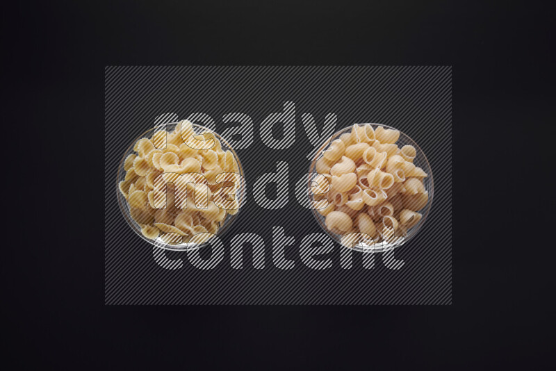 Different pasta types in glass bowls on black background