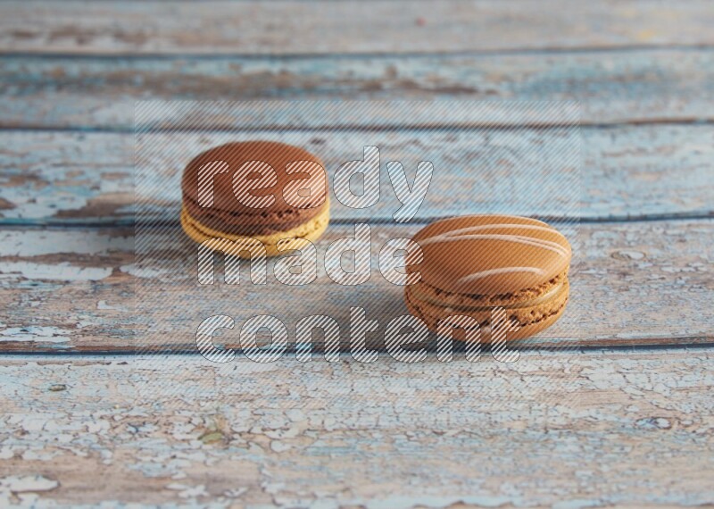 45º Shot of of two assorted Brown Irish Cream, and Yellow, and Brown Chai Latte macarons  on light blue background