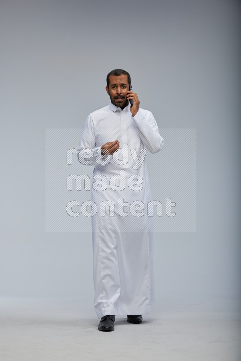 Saudi man wearing Thob standing talking on phone on Gray background