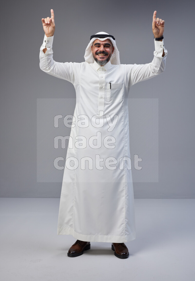 Saudi man Wearing Thob and white Shomag standing interacting with the camera on Gray background