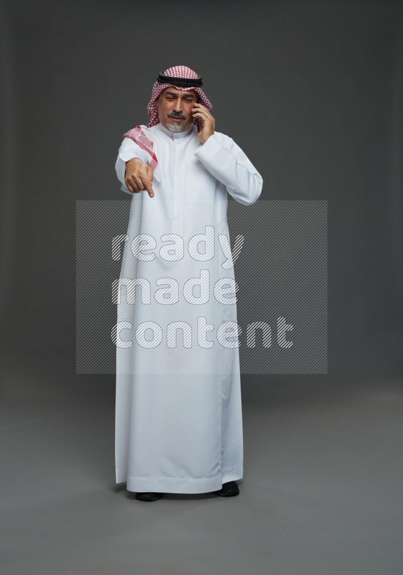 Saudi man with shomag Standing talking on phone on gray background