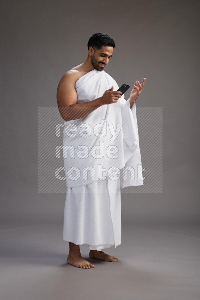A man wearing Ehram Standing texting on phone on gray background